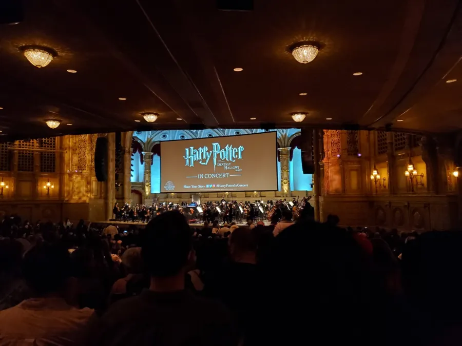 An orchestra on stage under the Harry Potter and the Deathly Hallows Part 2 in Concert screen, seen from the audience