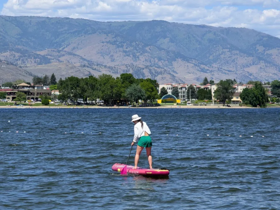 Rosie in a sun hat paddleboarding on a pink board out on a lake, with dry hills behind