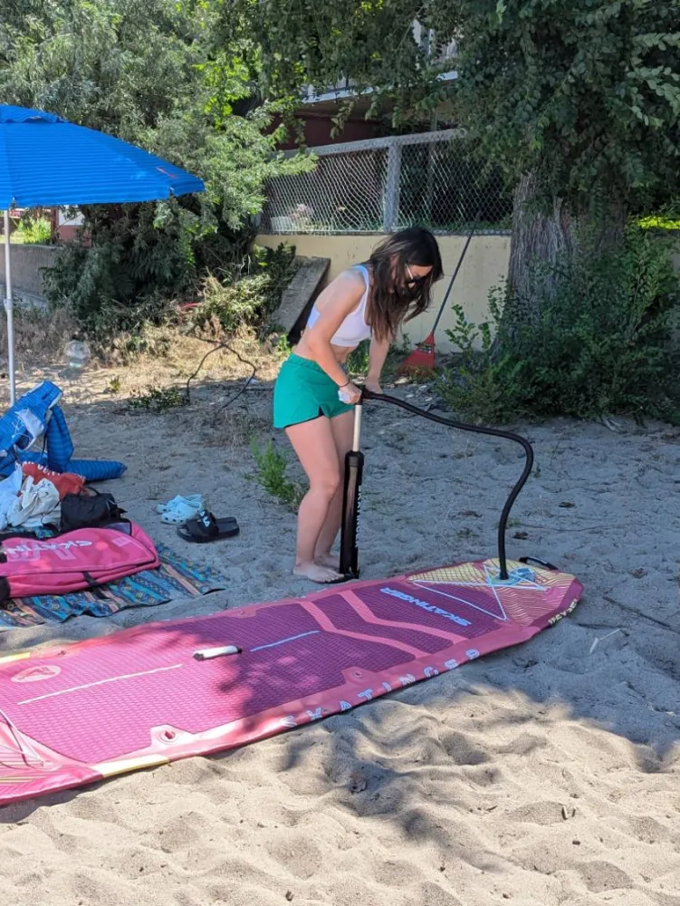 Rosie pumping up her pink inflatable paddleboard on a sandy beach